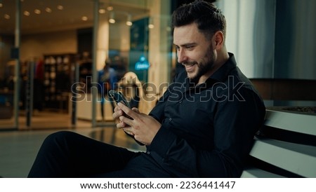Caucasian stylish man in black suit successful businessman customer sit at shopping mall using mobile phone apps make online order buying clothes win internet discounts chatting distant communication