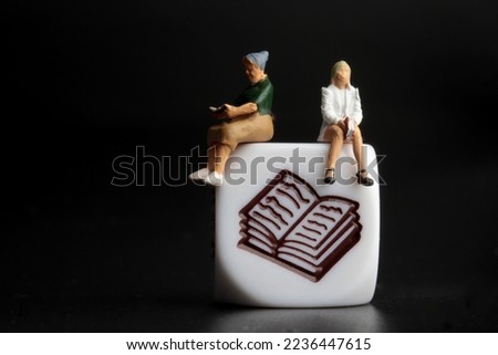 miniature figurines of two women reading a book sitting on a library symbol 