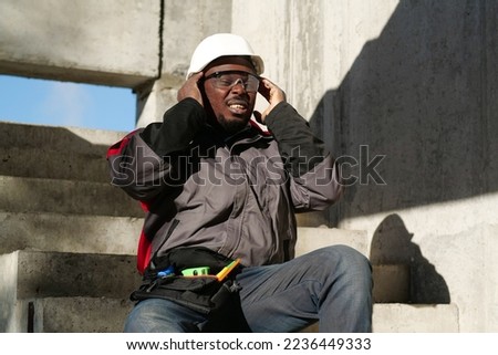 African american workman sits on the stairs of construction site. He is not feeling well and has headache, he massages his head Royalty-Free Stock Photo #2236449333