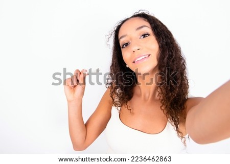 Beautiful teen girl with curly hair wearing white sport set over white background make selfie holding an invisible braces aligner, recommending this new treatment. Dental healthcare concept.