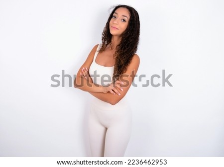 Portrait of Beautiful teen girl with curly hair wearing white sport set over white background standing with folded arms and smiling