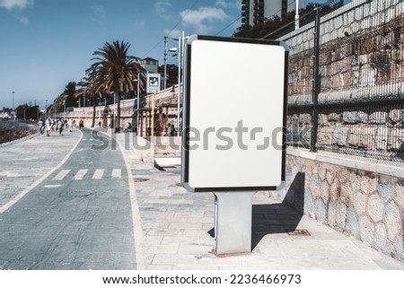 A vertical rectangular white empty advertising billboard template on the sidewalk; a mock-up of a blank advert poster placeholder in the pedestrian walk ; a mock up of an urban ad banner near the road