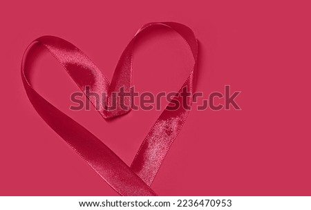 Heart shape from satin ribbon Valentine Day on red background with copy space. The image is colored in Viva Magenta Color of the Year 2023.