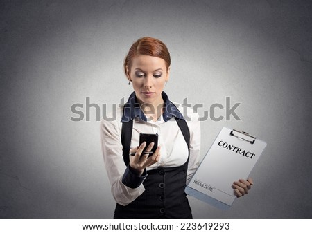 Portrait serious businesswoman signing holding contract document looking at reading news on smart mobile phone isolated grey wall background. Human face expression. Corporate employee executive