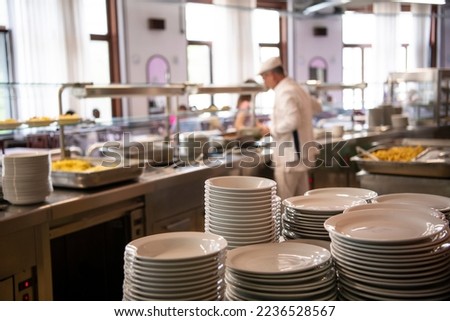 A pile of plates infront of Staff worker preparing food for students in school canteen. Lunch break. Education people and students school cafeteria. Belgrade, Serbia 17.05.2022
 Royalty-Free Stock Photo #2236528567