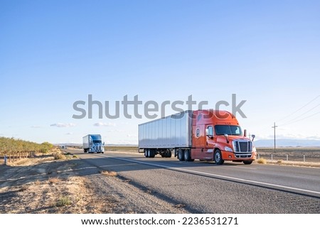 Industrial long hauler big rigs semi trucks team transporting commercial cargo in loaded dry van semi trailers running together on the flat straight highway road in California Royalty-Free Stock Photo #2236531271