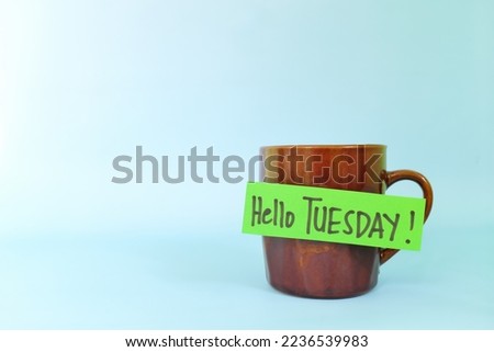 Welcome, hello and happy Tuesday concept. Selective focus of coffee cup with written message isolated in blue background.