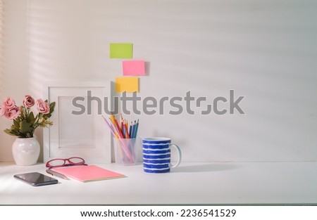 Comfortable workplace with picture frame flower pot, stationery and coffee cup on white table.