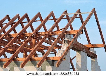 A timber roof truss, walls made of autoclaved aerated concrete blocks, a reinforced concrete beam and columns, a rough window opening, reinforced brick lintels, blue sky in the background Royalty-Free Stock Photo #2236554463