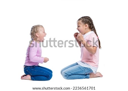 Two little girls are sitting and yelling at each other. Children in pink sweatshirts and jeans. Quarrel and emotions. Side view. Isolated on a white background.