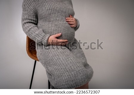 Cropped image of beautiful pregnant woman in cradle chair, holding pregnant belly and loving life, light background, place for text. Close up view	