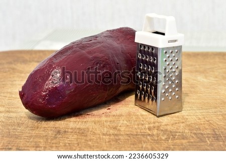 The picture shows a large red beet fruit and a small vegetable grater.