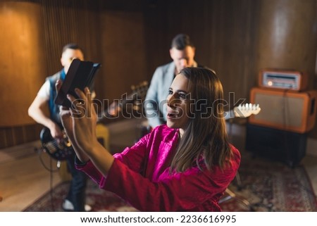cheerful singer-woman streaming a live video during repetition, other group members in the background music studio. High quality photo