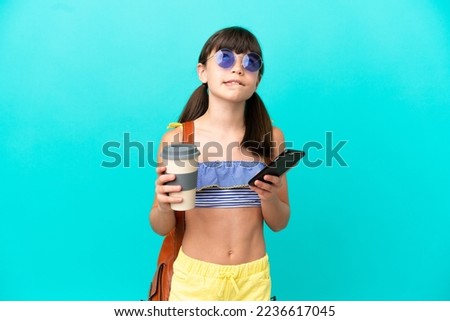 Little caucasian kid going to the beach isolated on blue background holding coffee to take away and a mobile while thinking something