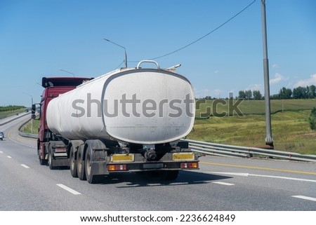 Red truck carrying tank semi-trailer on country road. Modern truck pulling white tank trailerswith combustible material through countryside in summer Royalty-Free Stock Photo #2236624849