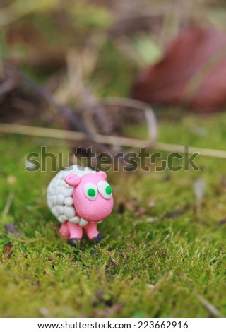 Plasticine world - little homemade white sheep with green eyes on a green background, selective focus and place for text