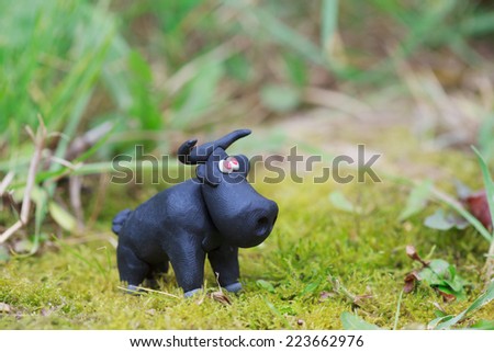 Plasticine world - little homemade black bull with red eyes on green background, selective focus