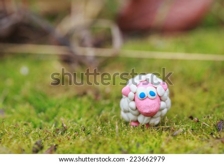 Plasticine world - little homemade white sheep with blue eyes on a green background, selective focus and place for text