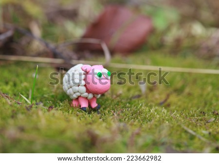 Plasticine world - little homemade white sheep with green eyes on a green background, selective focus and place for text 