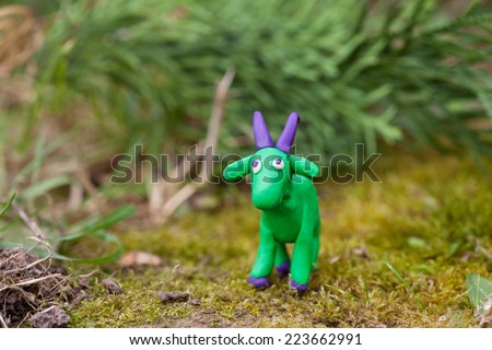 Plasticine world - little homemade green goat with purple horns and hooves on green background, selective focus and place for text