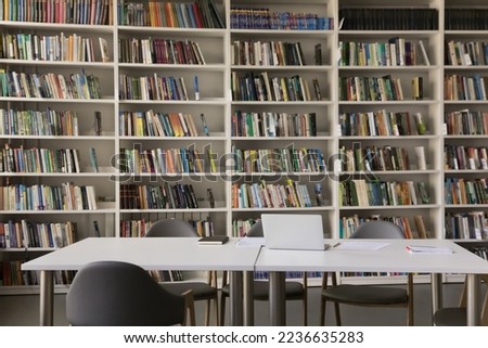 Public library interior with no people and bookshelves. Workplace table, desk with laptop and chairs for studying, college, university, high school students self preparation Royalty-Free Stock Photo #2236635283
