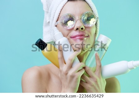 Vertical photo, a woman with clean white skin on a blue background in a towel on her head and body and beautiful glasses and patches on her lips shows her best cosmetics