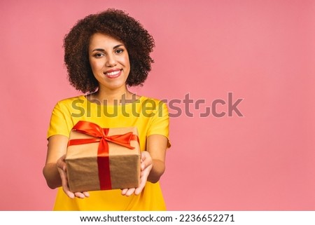 Happy young beautiful african american lady in casual laughing while holding present isolated over pink background.