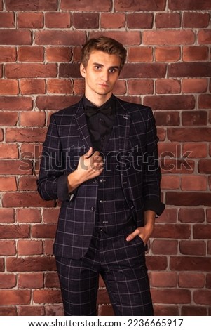 Portrait confident young businessman looking at camera at brick wall background. Stylish handsome man model in suit indoors. Caucasian male adult in studio. Fashion style concept. Copy space
