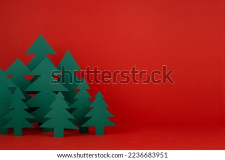 Traditional Christmas festive background with cartoon paper spruces as forest on red backdrop in elegant baby style, copy space, closeup. New Year  mockup for advertising, design, card, poster, flyer.