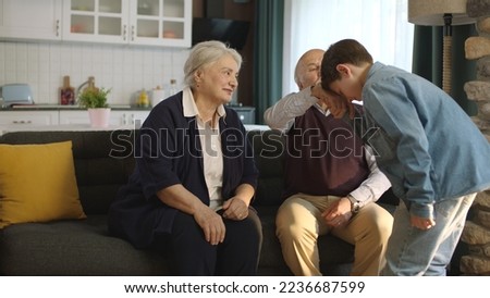 The little boy visited his grandfather and celebrated Eid al-Fitr by kissing their hands. Happy senior couple sitting on sofa kissing and hugging their little grandchild.  Royalty-Free Stock Photo #2236687599