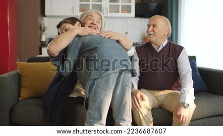 The little boy visited his grandfather and celebrated Eid al-Fitr by kissing their hands. Happy senior couple sitting on sofa kissing and hugging their little grandchild.  Royalty-Free Stock Photo #2236687607