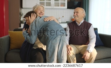 The little boy visited his grandfather and celebrated Eid al-Fitr by kissing their hands. Happy senior couple sitting on sofa kissing and hugging their little grandchild. 