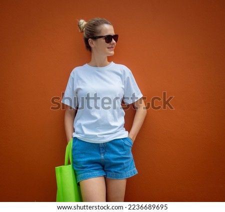 Female model wearing white blank t-shirt on the background of an orange wall.
