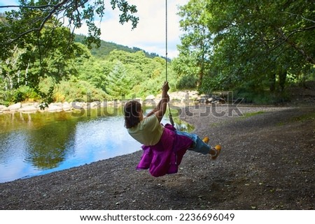 Jump into the water. A woman is resting on the lake. A swing from a rope and a stick. Active recreation in nature. Summer fun. A man is riding a swing.