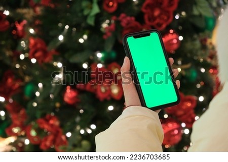 over the shoulder of hand holding green screen phone beside Christmas tree at night