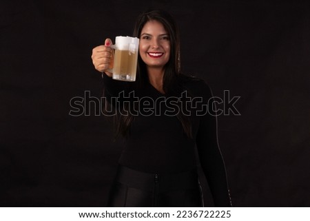 Beautiful, young woman holding a glass of cold beer, in black clothing on a black background.