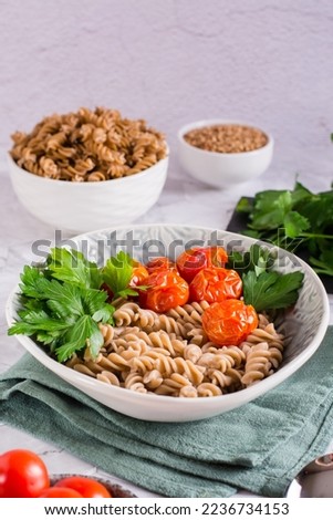 A bowl with buckwheat pasta, tomatoes and parsley leaves on the table. Vegetarian food. Vertical view