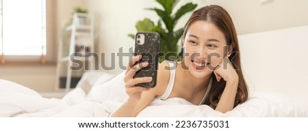 Attractive smile pretty asian young woman using and playing mobile phone, smartphone have video call or chat, lying down relax in bedroom wake up with covered blanket in cozy white bed in the morning