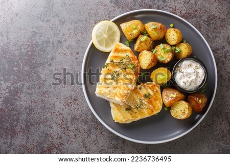 Grilled fish cod fillet with thyme served with baked potatoes, cream sauce and lemon on the table. Horizontal top view from above
