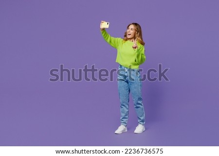 Full body young happy woman 30s she wearing casual green knitted sweater doing selfie shot on mobile cell phone post photo on social network isolated on plain pastel purple background studio portrait