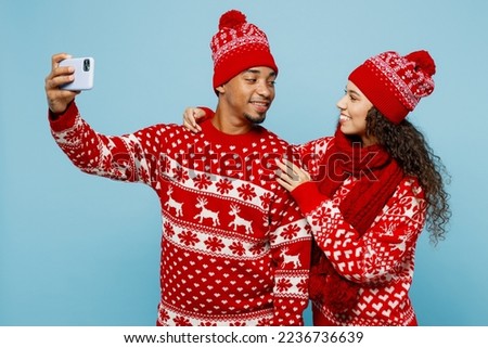 Merry young couple two man woman wear red Christmas sweater Santa hat posing doing selfie shot on mobile cell phone isolated on plain pastel light blue background. Happy New Year 2023 holiday concept