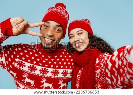 Close up merry young couple two man woman wear red Christmas sweater Santa hat posing do selfie shot pov on mobile cell phone isolated on plain pastel light blue background Happy New Year 2023 concept