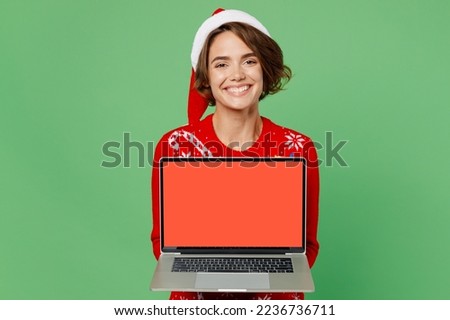 Merry fun young IT woman wear xmas sweater Santa hat posing work hold use laptop pc computer with blank screen area isolated on plain pastel light green background. Happy New Year 2023 holiday concept