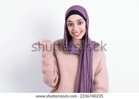 Lovely muslim woman wearing hijab and knitted sweater over white background pointing aside with forefinger, showing at copy space having news about bargains