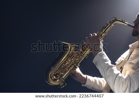 A European man plays the saxophone in the dark. Royalty-Free Stock Photo #2236744407