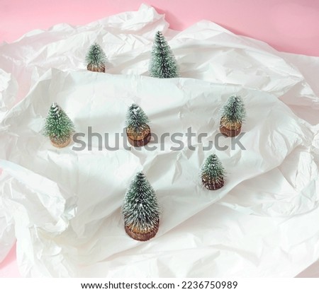 Crumpled white paper with small Christmas trees on pastel pink background. Minimal surreal creative concept for winter holidays banner or ad. Design for mountain ski resort ad or editorial. Concept