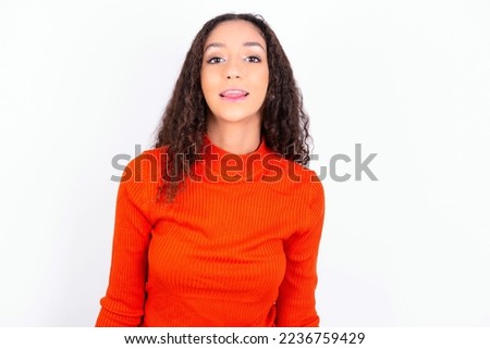 beautiful teen girl wearing knitted red sweater over white background with happy and funny face smiling and showing tongue.