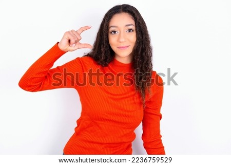 beautiful teen girl wearing knitted red sweater over white background smiling and gesturing with hand small size, measure symbol.
