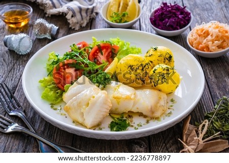 Fish dish - fried halibut with boiled potatoes and fresh vegetables on wooden table 