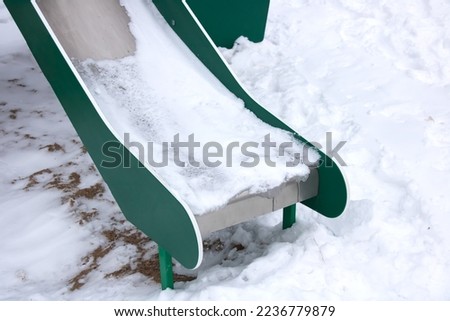 Green children's slide in the snow close up